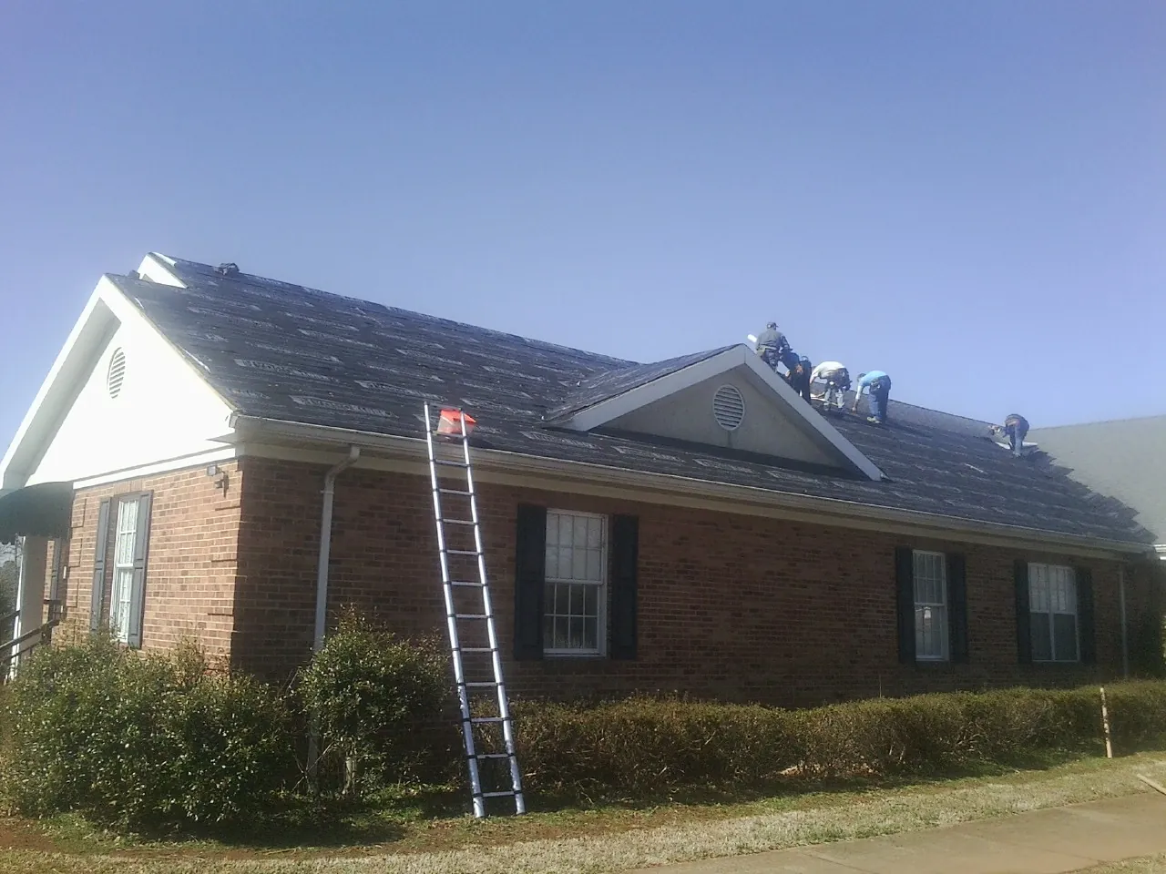 Crew tearing shingles off a brick ranch roof with a ladder set — Metal Roof Repair work by our crew in North Walpole