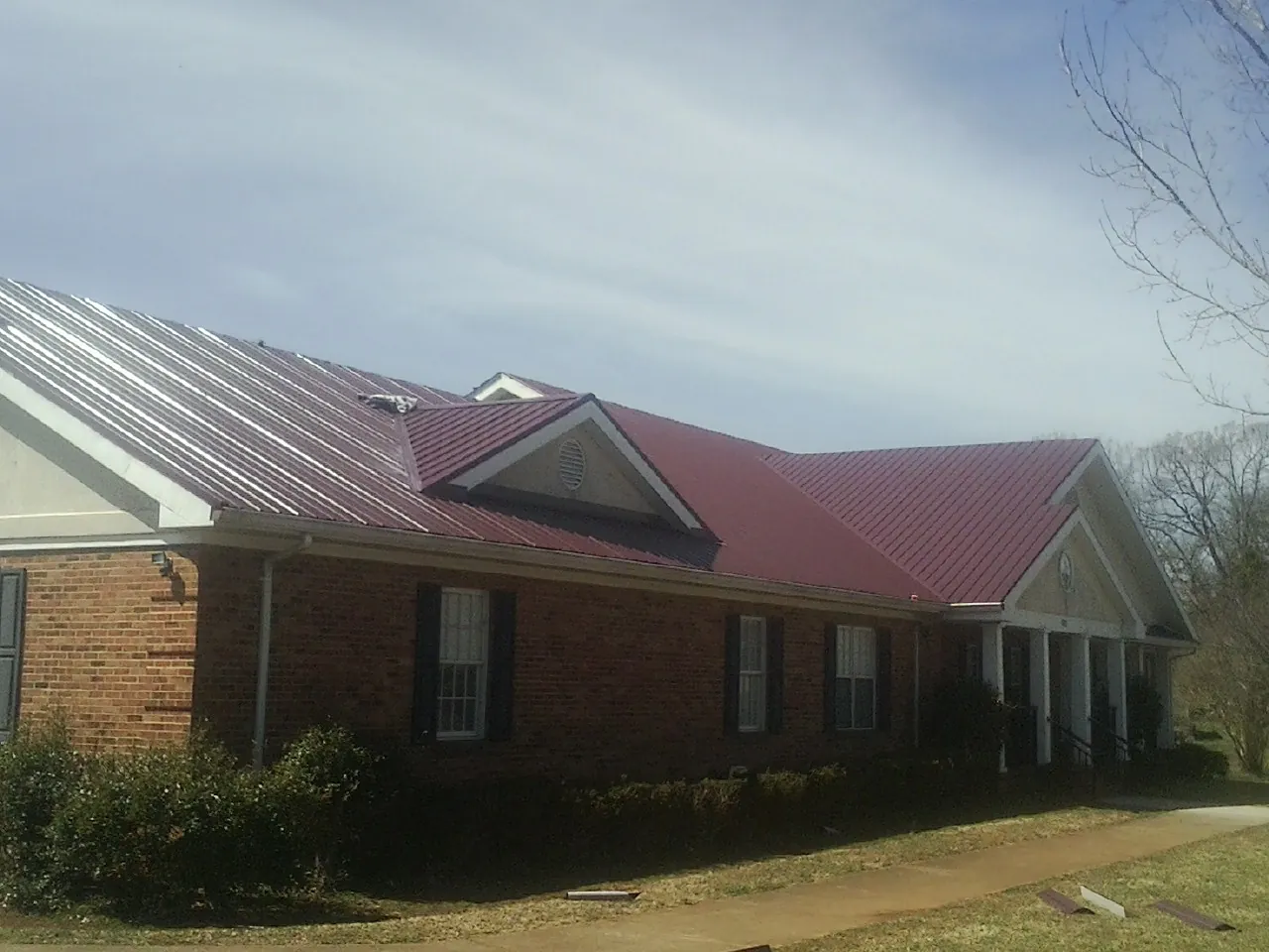 Red metal roof with gabled entries on a long brick building, from a Hail Damage Roof Repair job in North Walpole
