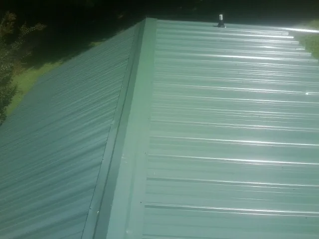 New green metal panels meeting at the ridge of a roof — Flat Roof Repair work by our crew in North Walpole