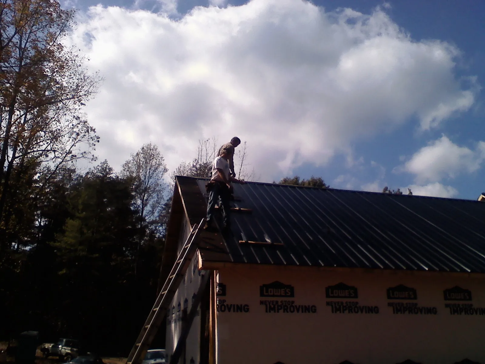 Roofer fastening dark metal panels high against a cloudy sky, from a Roof Inspection job in North Walpole