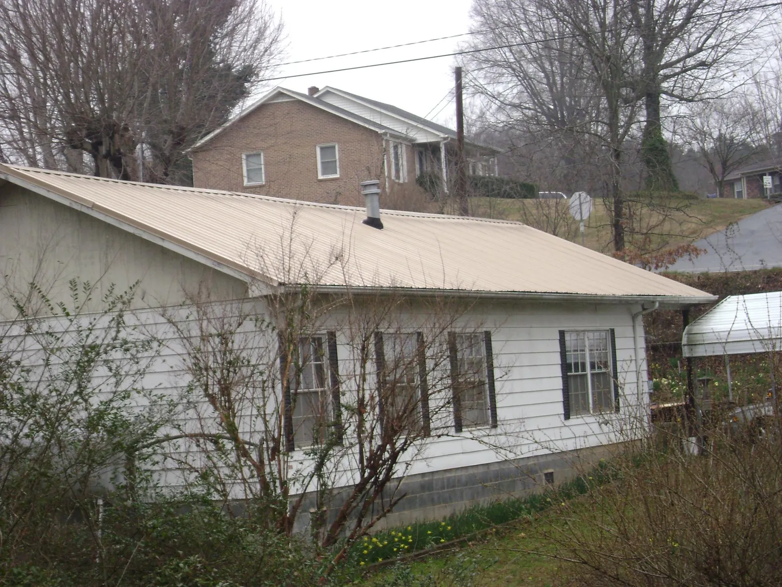 Tan metal roof on a white sided house set into a hillside — Commercial Roofing by Roofing Brothers in North Walpole